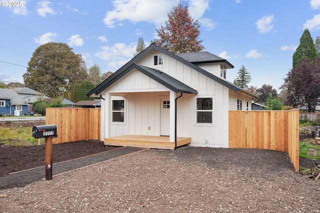 view of front facade featuring a shingled roof, board and batten siding, and fence