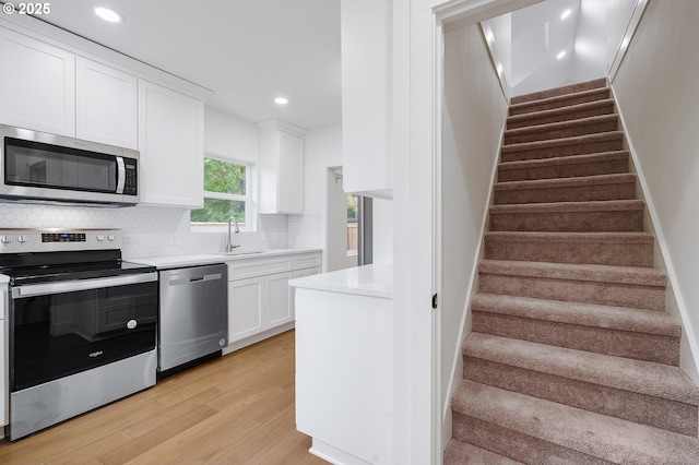 kitchen featuring decorative backsplash, light wood-type flooring, light countertops, white cabinetry, and appliances with stainless steel finishes