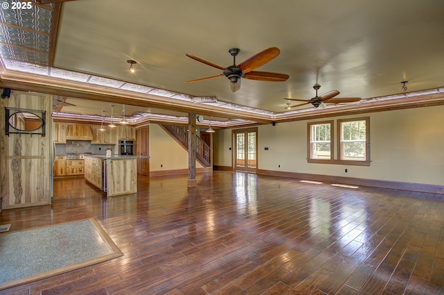 unfurnished living room featuring a tray ceiling, dark wood-type flooring, and ceiling fan