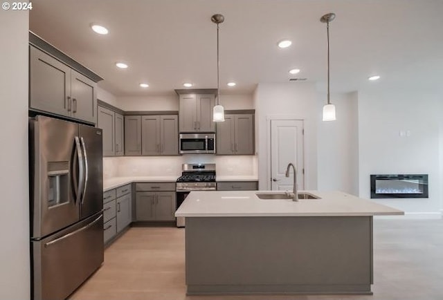 kitchen featuring decorative light fixtures, light countertops, appliances with stainless steel finishes, a sink, and an island with sink