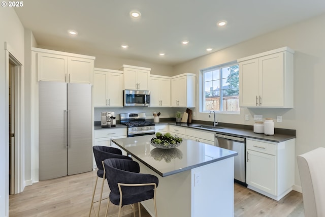 kitchen with a center island, stainless steel appliances, dark countertops, white cabinets, and a sink