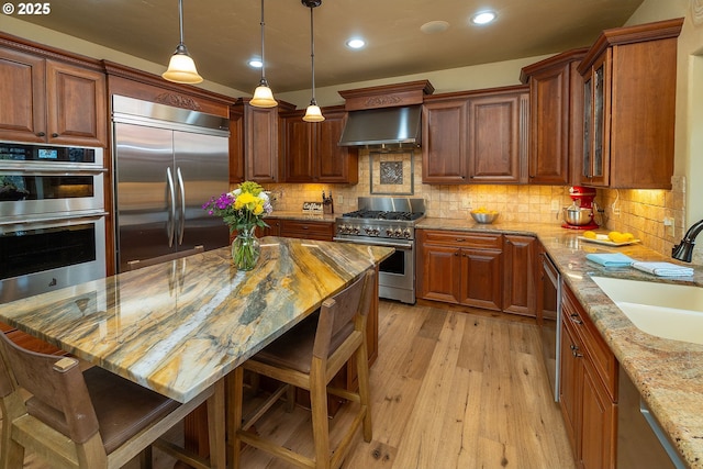 kitchen with high end appliances, a breakfast bar area, light stone countertops, wall chimney range hood, and a sink