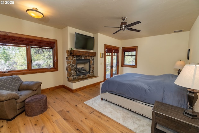 bedroom with access to exterior, wood-type flooring, multiple windows, and a fireplace