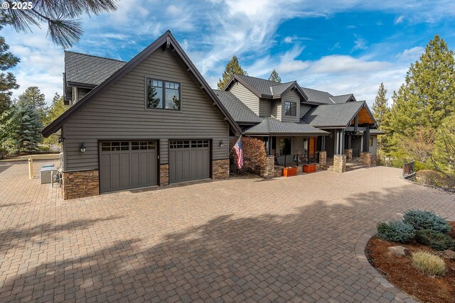 view of front of house featuring decorative driveway, a shingled roof, covered porch, an attached garage, and stone siding