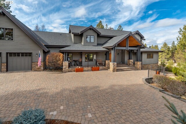 craftsman-style house featuring a garage, stone siding, decorative driveway, and covered porch