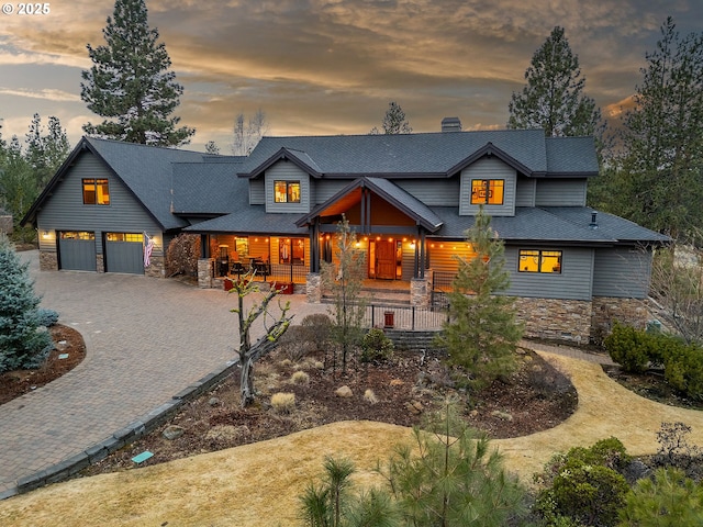 view of front of property featuring a porch, stone siding, decorative driveway, and an attached garage