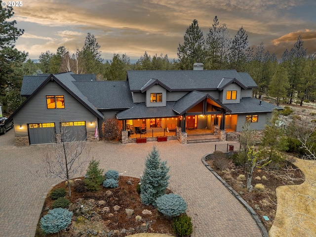 view of front facade with decorative driveway, covered porch, an attached garage, and stone siding