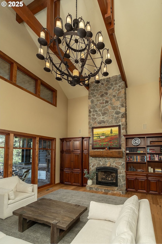 living area with beam ceiling, a fireplace, an inviting chandelier, wood finished floors, and high vaulted ceiling