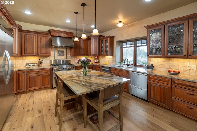 kitchen with light wood finished floors, decorative backsplash, wall chimney exhaust hood, appliances with stainless steel finishes, and light stone countertops