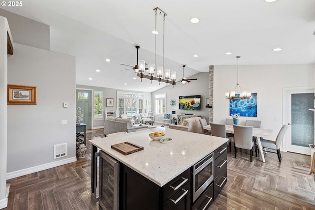 kitchen featuring beverage cooler, ceiling fan with notable chandelier, visible vents, dark cabinetry, and stainless steel microwave