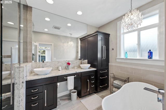 full bath with double vanity, a soaking tub, tile walls, and a sink