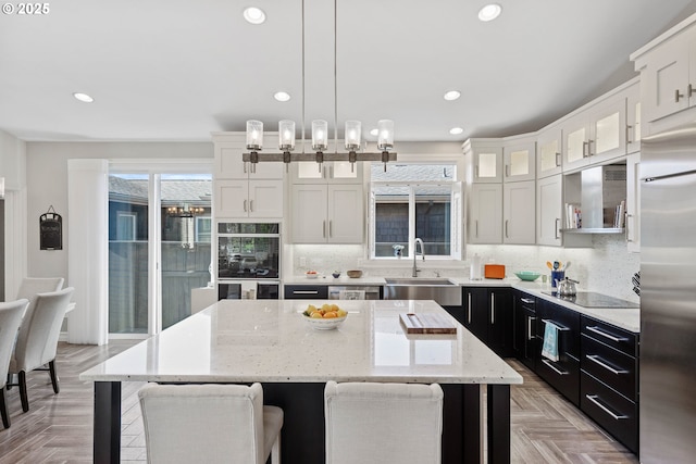 kitchen featuring tasteful backsplash, a kitchen island, dark cabinetry, black appliances, and a sink