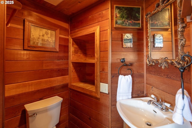 bathroom featuring a sink, wooden walls, and toilet