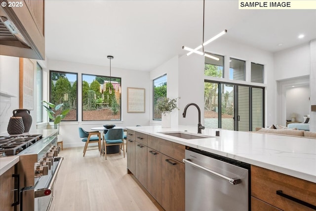 kitchen with stainless steel appliances, a sink, light wood-style floors, light stone counters, and brown cabinetry