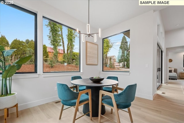 dining space with a chandelier, light wood-type flooring, healthy amount of natural light, and baseboards