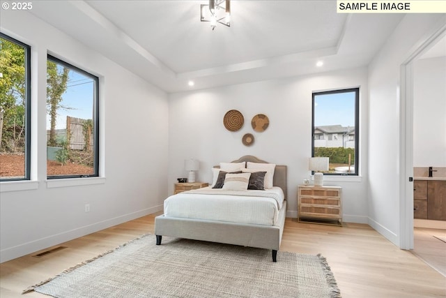 bedroom with light wood-type flooring, recessed lighting, baseboards, a tray ceiling, and connected bathroom