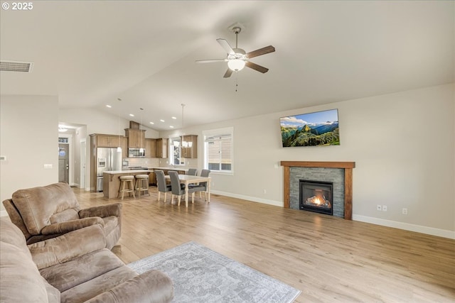 living room with lofted ceiling, a stone fireplace, light hardwood / wood-style floors, and ceiling fan