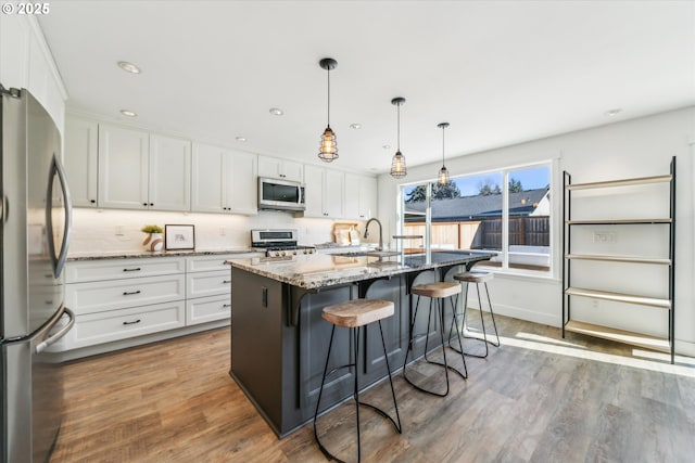 kitchen with stainless steel appliances, white cabinetry, light stone countertops, and a center island with sink