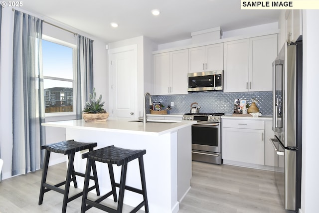 kitchen with a sink, decorative backsplash, light countertops, appliances with stainless steel finishes, and a kitchen bar