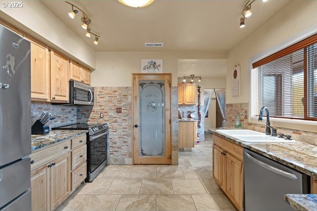 kitchen with sink, stainless steel appliances, light stone countertops, light brown cabinetry, and decorative backsplash