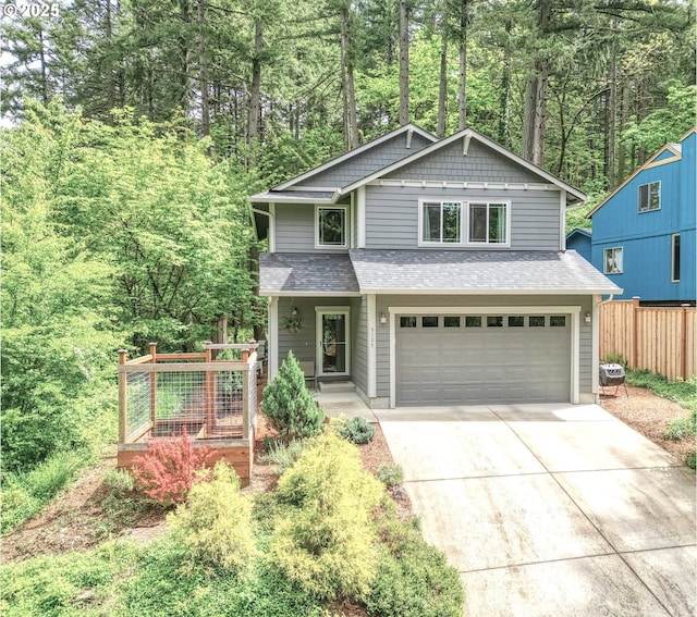 view of front facade with fence, a shingled roof, a garage, concrete driveway, and a forest view