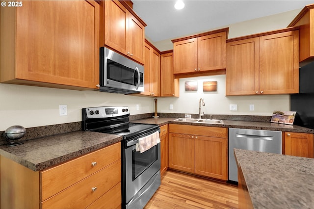 kitchen with a sink, dark countertops, stainless steel appliances, and light wood-type flooring