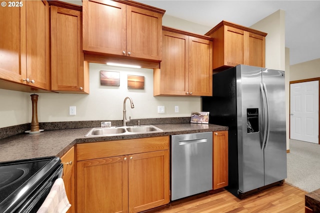 kitchen with brown cabinetry, dark countertops, a sink, stainless steel appliances, and light wood-style flooring