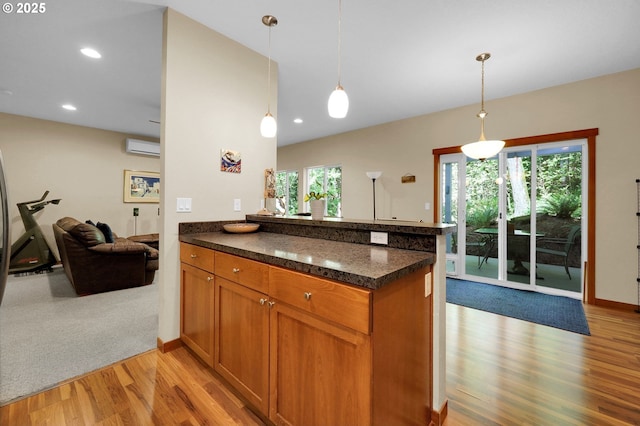 kitchen with brown cabinets, light wood finished floors, an AC wall unit, a peninsula, and open floor plan