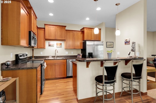 kitchen with appliances with stainless steel finishes, a sink, light wood finished floors, and a kitchen bar