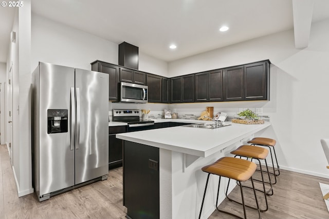 kitchen featuring light wood-style flooring, a kitchen bar, appliances with stainless steel finishes, and a sink