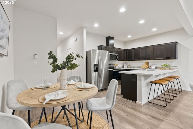 kitchen with a breakfast bar area, stainless steel appliances, light countertops, light wood-style flooring, and a peninsula