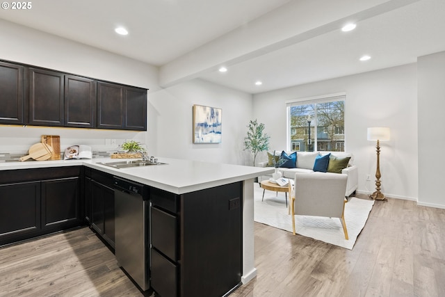 kitchen with light countertops, light wood-style flooring, a sink, dishwasher, and a peninsula