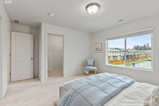 carpeted bedroom with baseboards, visible vents, a walk in closet, and a textured ceiling