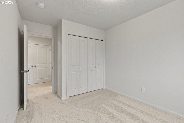 unfurnished bedroom with a closet, light carpet, a textured ceiling, and baseboards