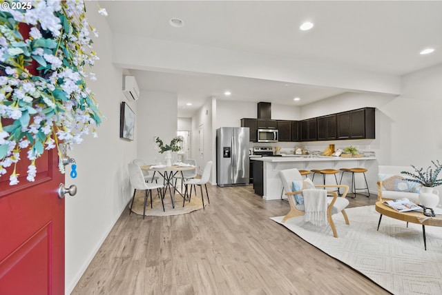 kitchen featuring stainless steel appliances, light countertops, a wall mounted AC, light wood-type flooring, and a peninsula