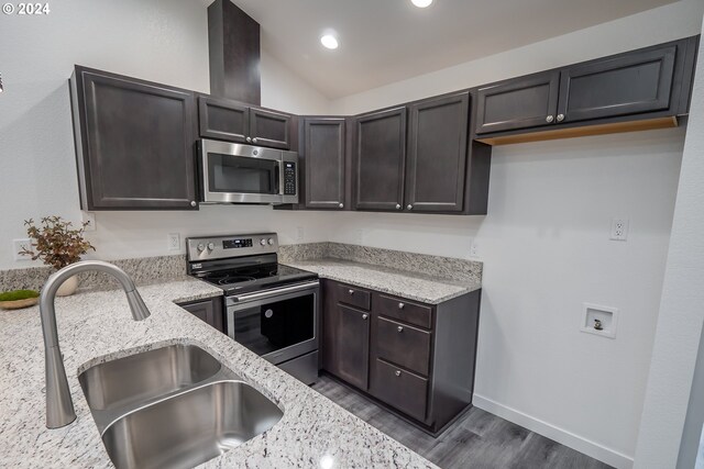 kitchen featuring lofted ceiling, sink, appliances with stainless steel finishes, dark brown cabinets, and light stone countertops