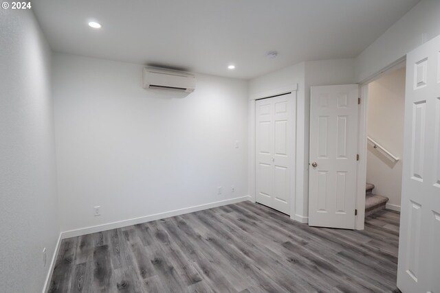 unfurnished bedroom with hardwood / wood-style floors, a wall unit AC, and a closet