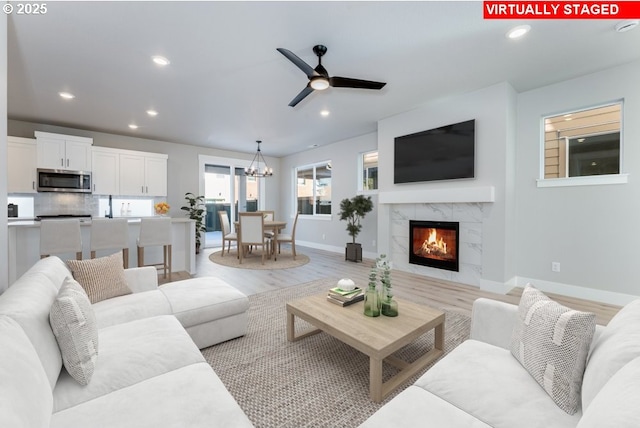 living room with ceiling fan with notable chandelier, a fireplace, and light hardwood / wood-style floors