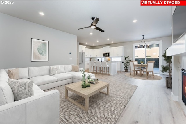 living room with ceiling fan with notable chandelier and light hardwood / wood-style floors