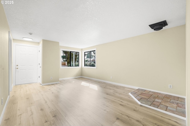 empty room featuring light wood finished floors, a textured ceiling, and baseboards