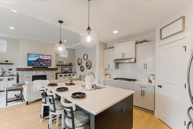 12505 NE 102nd Way, Vancouver, WA 98682 - kitchen with under cabinet range hood, stainless steel gas stovetop, light wood finished floors, a kitchen bar, and decorative backsplash