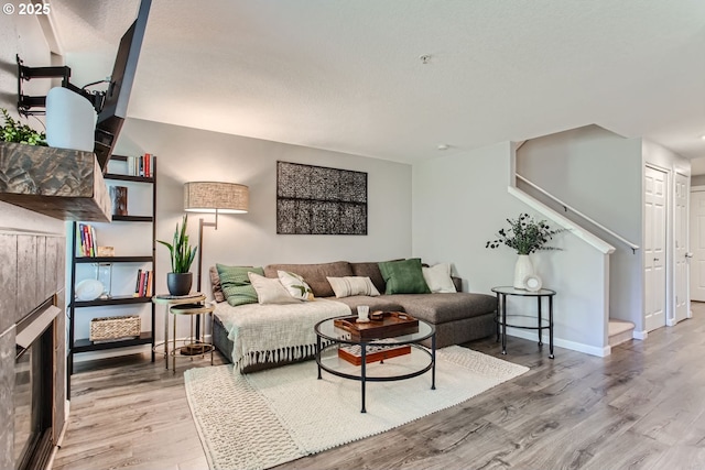 living area featuring stairway, light wood-type flooring, a fireplace, and baseboards