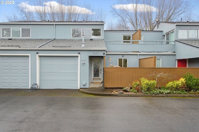 view of property with fence, a garage, and a shingled roof