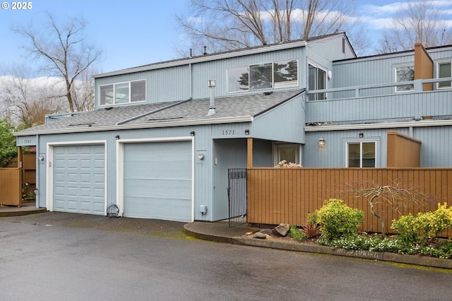 townhome / multi-family property with roof with shingles, a balcony, and fence