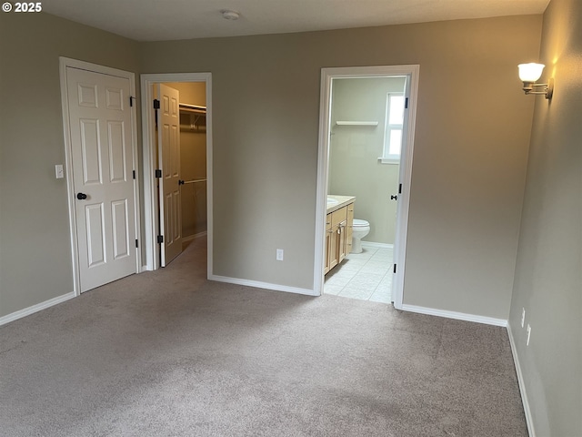 unfurnished bedroom featuring a walk in closet, light colored carpet, ensuite bath, and a closet