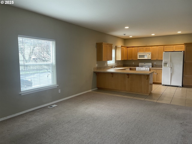 kitchen with a breakfast bar, light colored carpet, plenty of natural light, kitchen peninsula, and white appliances