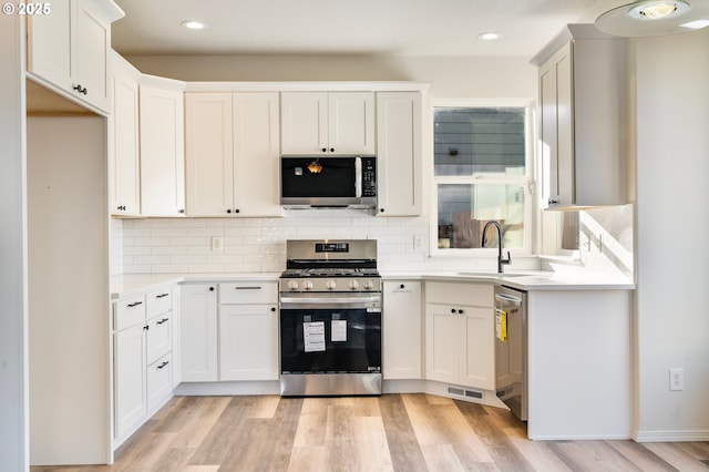 kitchen with white cabinetry, decorative backsplash, light hardwood / wood-style flooring, and appliances with stainless steel finishes