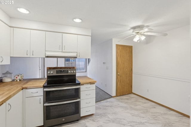 kitchen with marble finish floor, white cabinetry, under cabinet range hood, range with two ovens, and wood counters