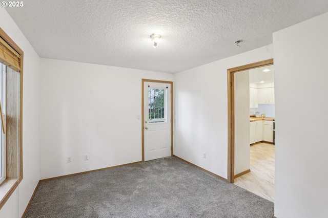 unfurnished room featuring light colored carpet, a textured ceiling, and baseboards