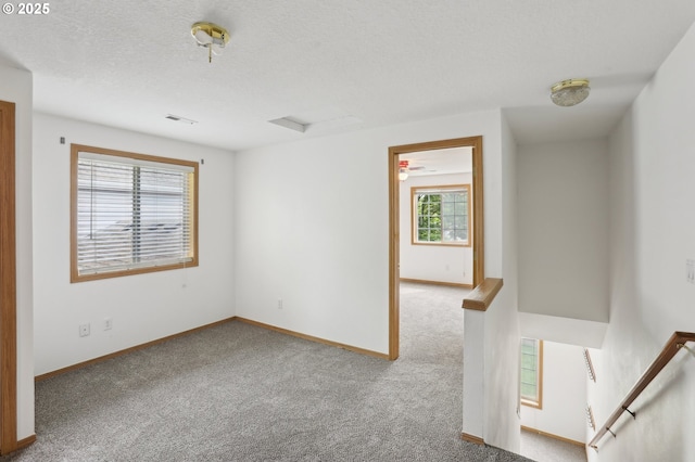 unfurnished room featuring a textured ceiling, baseboards, visible vents, and carpet
